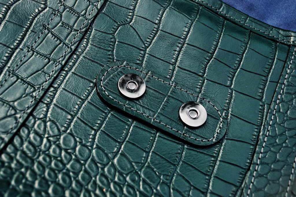 Close-up of a green textured leather bag with metal buttons.
