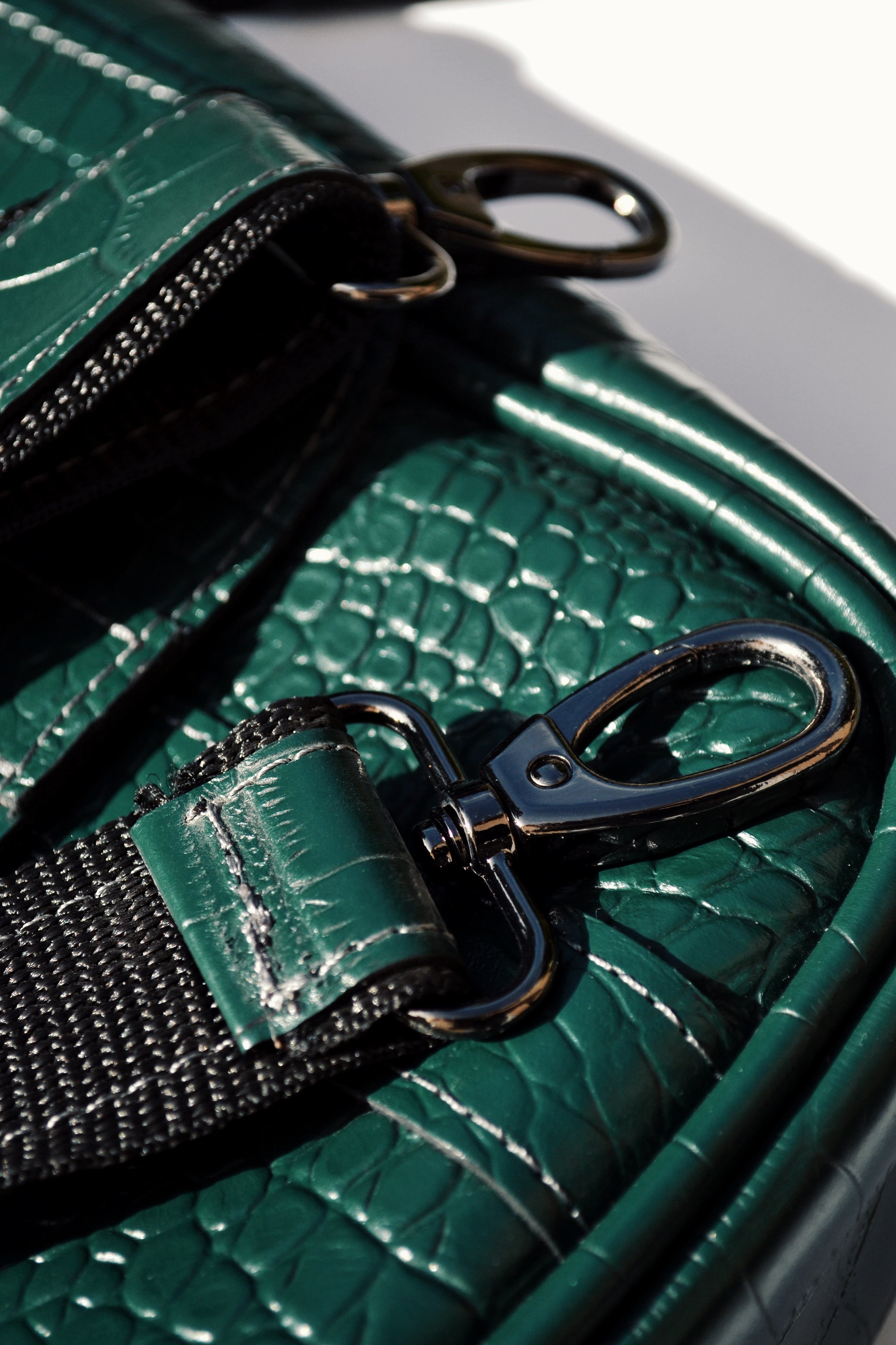 Close-up of a green textured handbag with a black strap and clasp.